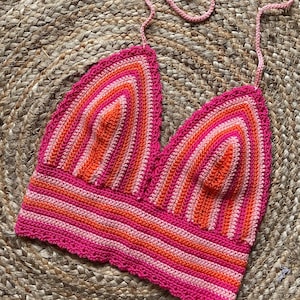 Può includere: Top all'uncinetto fatto a mano nei toni del rosa e dell'arancione. Il top presenta un design all'americana con bordo smerlato e motivo a righe. Misura circa 30 cm di larghezza ed è perfetto per l'estate.