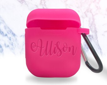 May include: A bright pink silicone case for wireless earbuds with a carabiner clip. The case has the name "Allison" embossed on the front.