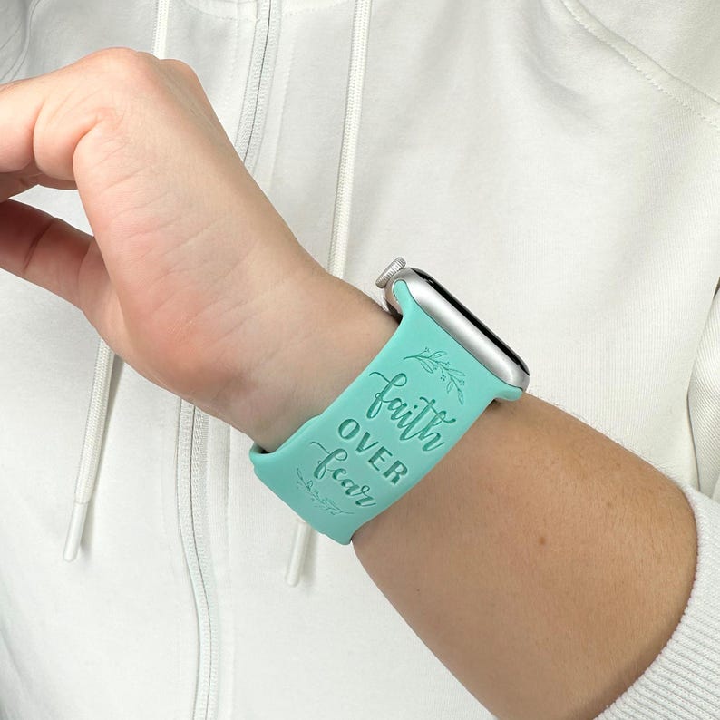 May include: A turquoise blue Apple Watch band with the text "faith over fear" in white lettering. The band is made of silicone and has a smooth finish.