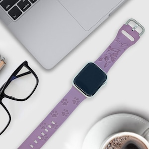 K&ouml;nnte beinhalten: Ein lilafarbenes Silikonarmband f&uuml;r die Apple Watch mit einem Pfotenabdruck-Design und dem Wort "Snuggle" in Pr&auml;gung auf dem Armband.