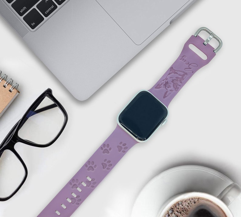 K&ouml;nnte beinhalten: Ein lilafarbenes Silikonarmband f&uuml;r die Apple Watch mit einem Pfotenabdruck-Design und dem Wort "Snuggle" in Pr&auml;gung auf dem Armband.