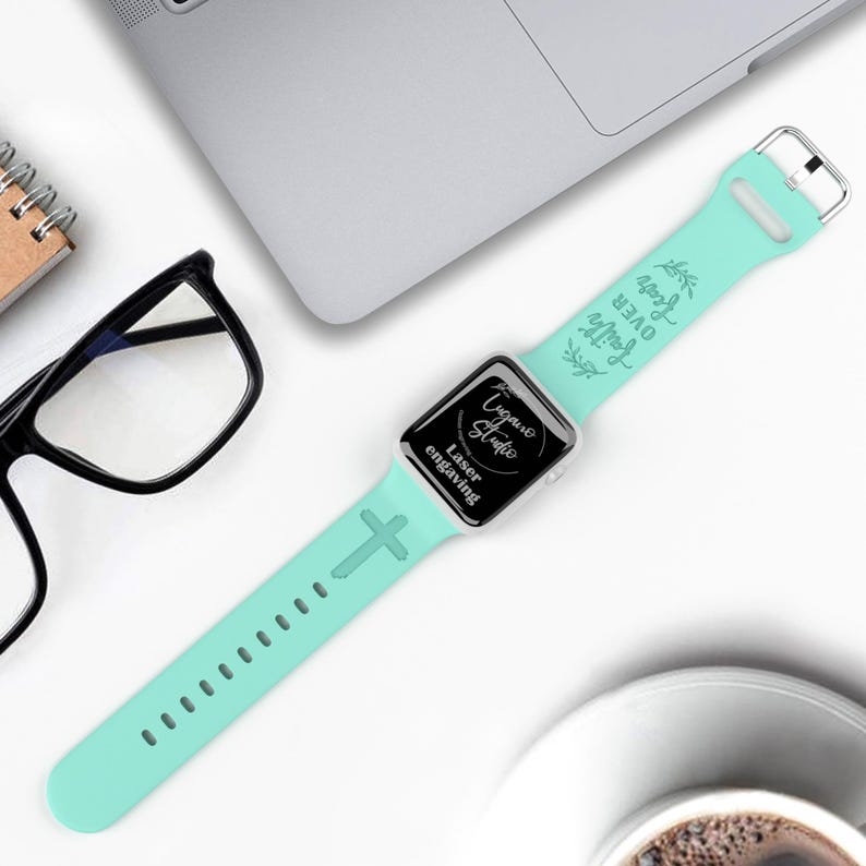 May include: A light blue Apple Watch band with a cross design and the words "Love Over All" engraved on it. The band is made of silicone and is compatible with Apple Watch Series 4 and later.