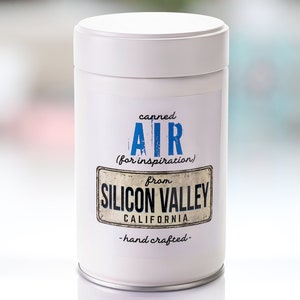 May include: A white cylindrical can with a blue and black label that reads "Canned Air (for inspiration) from Silicon Valley California - hand crafted - "