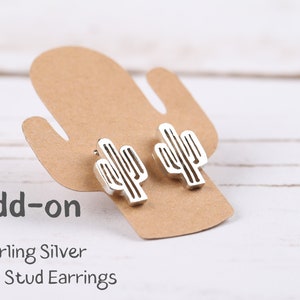 May include: Add-on Sterling Silver Cactus Stud Earrings. Two silver cactus earrings are displayed on a brown card shaped like a cactus.