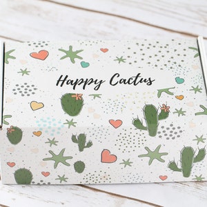May include: A white cardboard box with a colorful pattern of cacti, stars, and hearts. The box has the text "Happy Cactus" printed on it.
