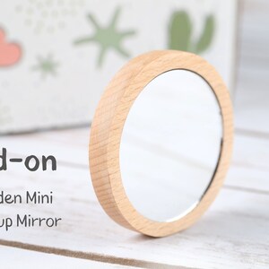 May include: Add-on Wooden Mini Makeup Mirror. A small, round mirror with a wooden frame.