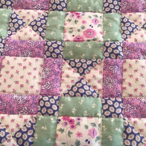 Op de afbeelding: Een patchworkdeken met verschillende bloemenpatronen in roze, groene en witte tinten.