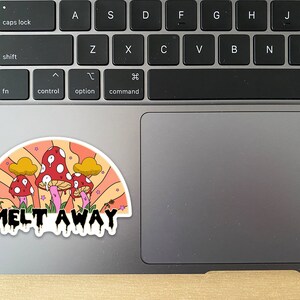 K&ouml;nnte beinhalten: Ein farbenfroher Aufkleber mit einem skurrilen Design von roten Pilzen mit wei&szlig;en Punkten, vor einem Regenbogenhintergrund im Retro-Stil. Der Aufkleber tr&auml;gt den Text "MELT AWAY" in einer tropfenden Schriftart. Der Aufkleber befindet sich auf einem Laptop.