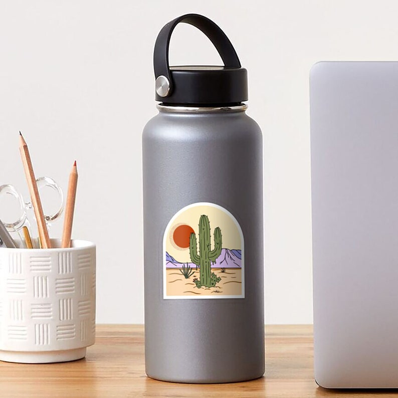 Pu&ograve; includere: Un adesivo raffigurante un paesaggio desertico con un cactus verde, un sole al tramonto e montagne viola. Il design &egrave; incorniciato in un arco color crema, evocando un'estetica vintage. L'adesivo &egrave; su una borraccia argentata.