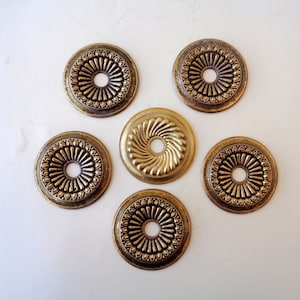 Könnte beinhalten: Sechs antike Deckenrosetten aus Messing. Fünf sind kreisförmig mit einem Blumendesign am Rand und einem zentralen Loch. Die sechste Rosette ist goldfarbener mit einem Spiraldesign.