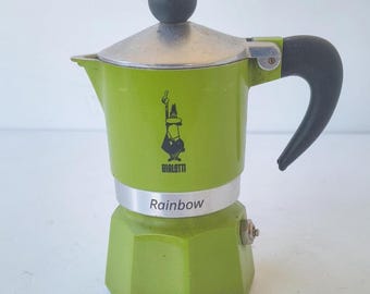 May include: A green stovetop espresso maker with a black handle and knob. The word "Bialetti" is printed on the front, along with a logo. The word "Rainbow" is printed on the base of the coffee maker.