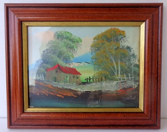 Könnte beinhalten: Ölgemälde einer ländlichen Landschaft mit einem Gebäude mit rotem Dach, umgeben von grünen Bäumen und blauem Himmel. Das Kunstwerk ist in einem dunkelbraunen Holzrahmen mit goldenem Innenrand gerahmt.