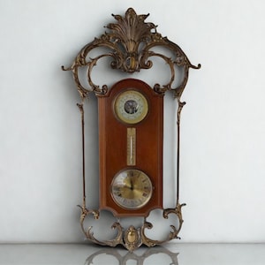 May include: An antique wall-mounted weather station with a dark wood panel and ornate bronze-colored metal frame. The station includes a barometer, thermometer, and clock with a gold-colored face. The frame features decorative scrollwork and a stylized top.