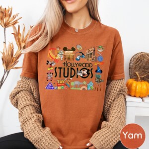 A woman wearing a t-shirt with various Disney and Hollywood-themed graphics, including Mickey Mouse, Minnie Mouse, and other iconic characters, along with the text "Hollywood STUDIOS" and "Toy Story Land".