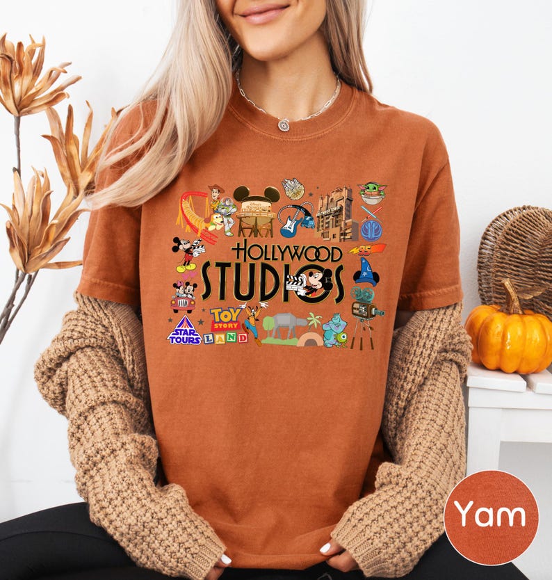 A woman wearing a t-shirt with various Disney and Hollywood-themed graphics, including Mickey Mouse, Minnie Mouse, and other iconic characters, along with the text "Hollywood STUDIOS" and "Toy Story Land".