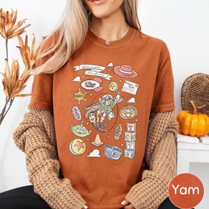 A woman wearing a brown t-shirt with a cartoon character design and various other cartoon-related icons, along with a necklace and a sweater.
