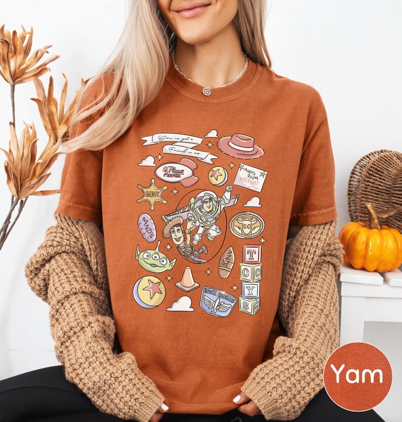 A woman wearing a brown t-shirt with a cartoon character design and various other cartoon-related icons, along with a necklace and a sweater.
