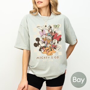 A woman wearing a t-shirt with a graphic of Disney characters, specifically Mickey Mouse and Donald Duck, along with the text "Mickey & Co" and "Est. 1928".