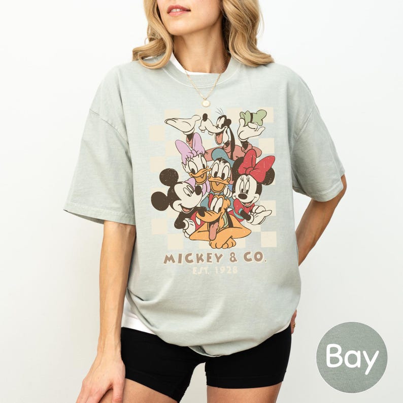A woman wearing a t-shirt with a graphic of Disney characters, specifically Mickey Mouse and Donald Duck, along with the text "Mickey & Co" and "Est. 1928".