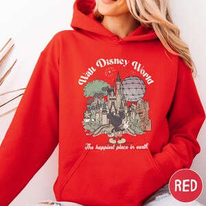 A woman wearing a red hoodie with a graphic of Disney World and the text "The happiest place in earth" printed on it.