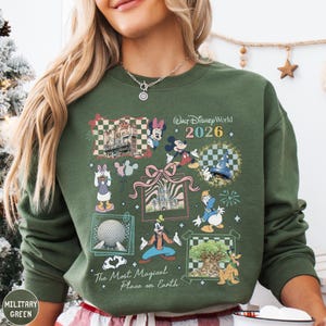 A woman wearing a green sweatshirt with a collage of Disney characters and landmarks, including Mickey Mouse, Minnie Mouse, Goofy, and the Eiffel Tower, along with the text "Disney World 2026" and "The Most Magical Place on Earth".