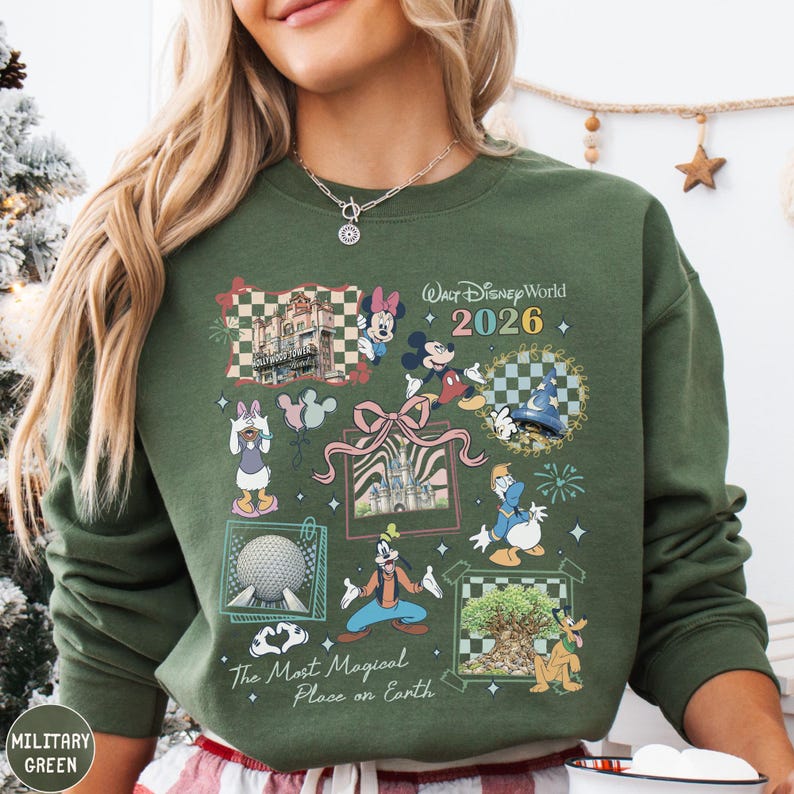 A woman wearing a green sweatshirt with a collage of Disney characters and landmarks, including Mickey Mouse, Minnie Mouse, Goofy, and the Eiffel Tower, along with the text "Disney World 2026" and "The Most Magical Place on Earth".