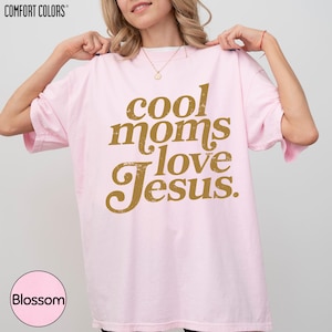 A woman wearing a pink t-shirt with the text "cool moms love Jesus" printed on it.