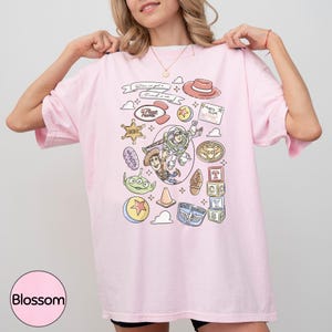 A woman wearing a pink t-shirt with various cartoon characters and icons printed on it, including a character from the Toy Story franchise.