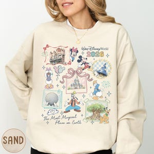 A woman wearing a beige sweater with a collage of Disney-themed illustrations and text, including characters like Minnie Mouse, Mickey Mouse, Donald Duck, and Goofy.