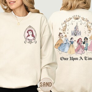 A woman wearing a white sweatshirt with a Disney princess design on the front and a back featuring a castle and the text "Once Upon a Time" on the back.