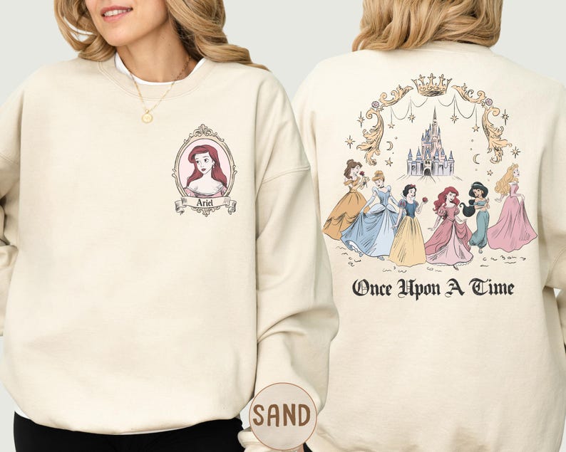 A woman wearing a white sweatshirt with a Disney princess design on the front and a back featuring a castle and the text "Once Upon a Time" on the back.
