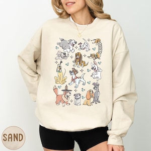 May include: Sand-colored sweatshirt featuring a collection of cartoon dog illustrations. The dogs are in various poses and styles, with heart and star accents. The sweatshirt has a crew neck and long sleeves.