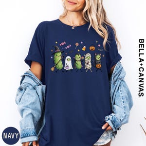 A woman wearing a navy blue t-shirt with a Halloween-themed graphic of various cartoon characters, including a witch, ghost, mummy, pumpkin, and candy cane.