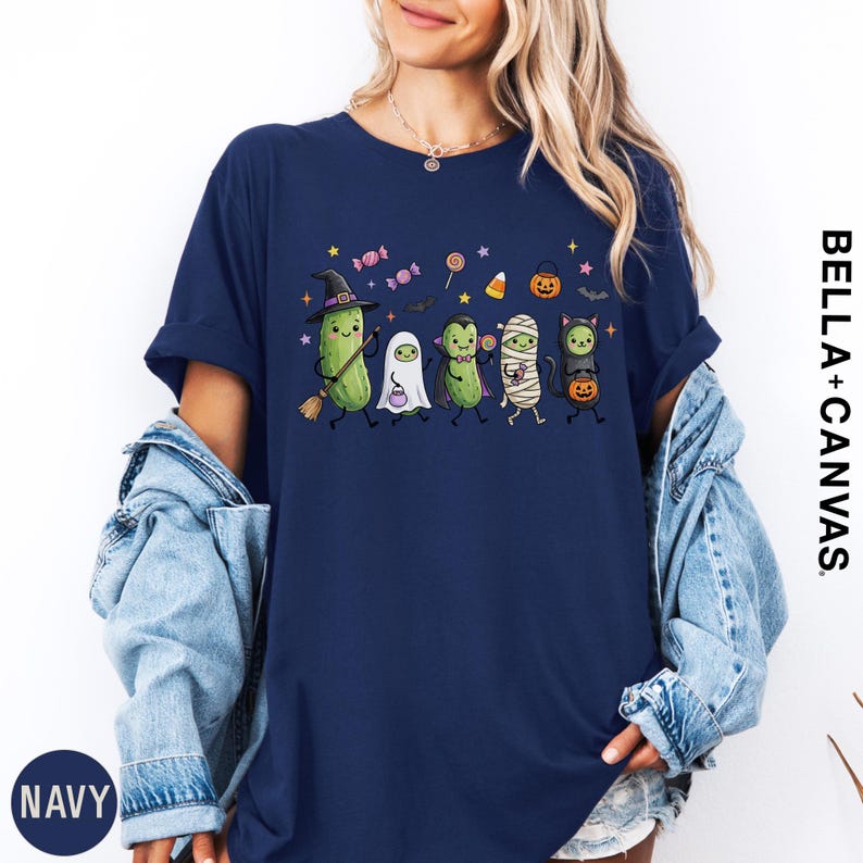 A woman wearing a navy blue t-shirt with a Halloween-themed graphic of various cartoon characters, including a witch, ghost, mummy, pumpkin, and candy cane.