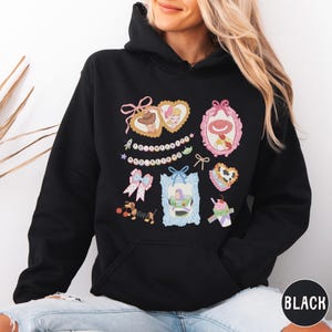 A woman wearing a black hoodie with a colorful graphic design featuring various cartoon-style illustrations and text.
