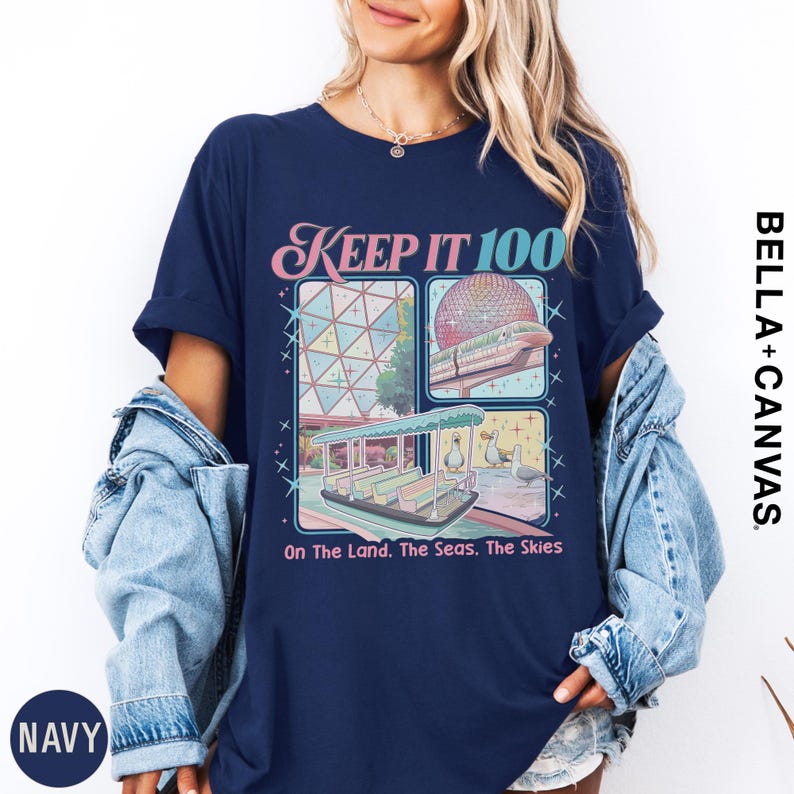 A woman wearing a navy blue t-shirt with a graphic design featuring a collage of images related to the Disney theme park, including a Ferris wheel, a boat, and a beach scene.