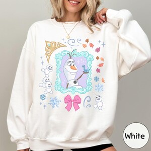 A woman wearing a white sweater with a colorful graphic design featuring characters from the Disney movie Frozen.