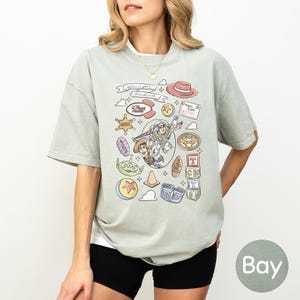 A woman wearing a t-shirt with a graphic design featuring various cartoon characters and icons, including a character from the Toy Story franchise.
