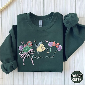 A green sweatshirt with a colorful graphic design featuring a cartoon character and the text "Part of your world" printed on it.