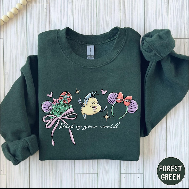 A green sweatshirt with a colorful graphic design featuring a cartoon character and the text "Part of your world" printed on it.