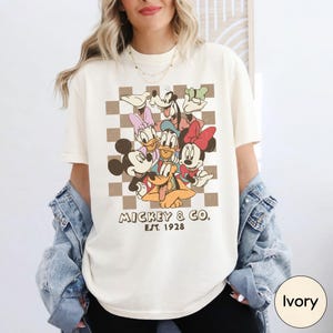 A woman wearing a white t-shirt with a graphic of Disney characters and text below it.