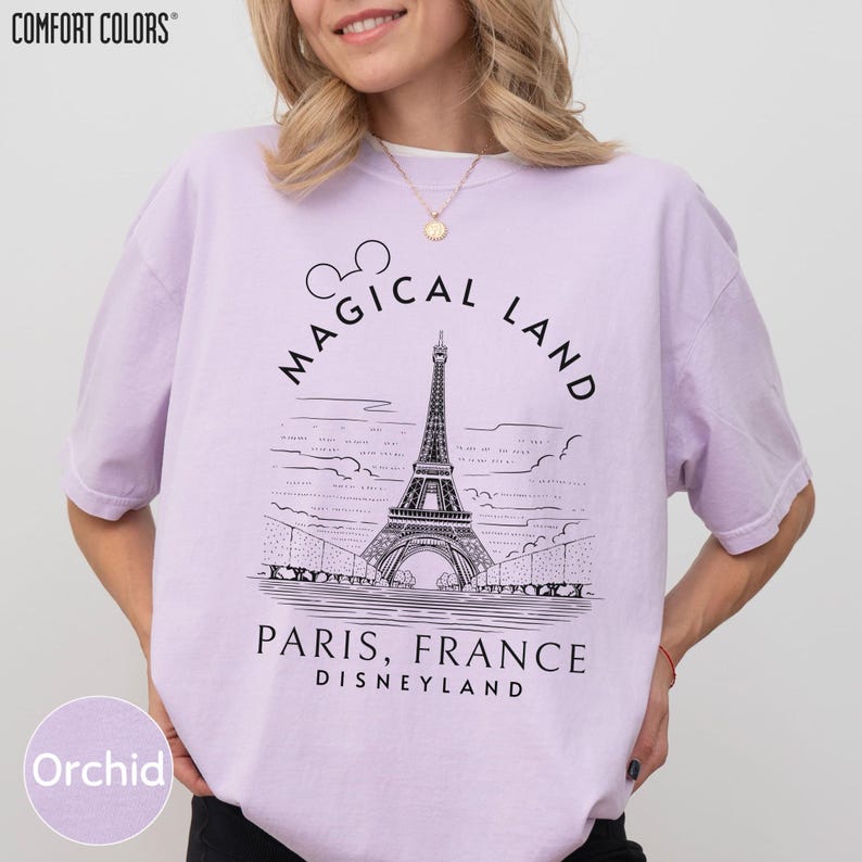 A woman wearing a purple t-shirt with a graphic design of the Eiffel Tower and the text "Magical Land Paris, France Disneyland" printed on it.