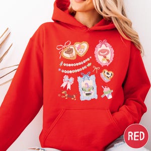 A woman wearing a red hoodie with various cartoon-style illustrations and text on it.
