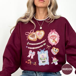 A woman wearing a burgundy sweatshirt with various cartoon-style illustrations and text on it.