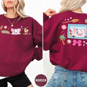 A woman wearing a burgundy sweatshirt with a cartoon pig design and various other decorative elements.
