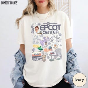 A woman wearing a white t-shirt with various Disney-themed graphics and text, including the words "EPcot Center" and "Disney World".