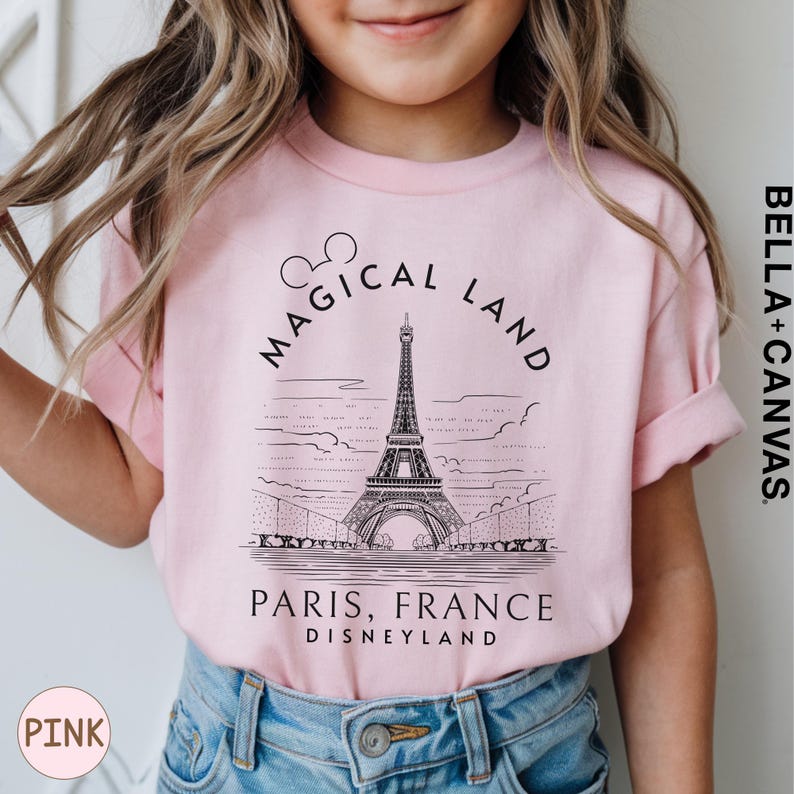 A young girl wearing a pink t-shirt with a graphic of the Eiffel Tower and text that says "Magical Land Paris, France Disneyland".
