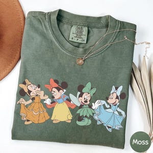 a green t-shirt with a graphic of Minnie Mouse and Snow White, along with a necklace and a brown hat.