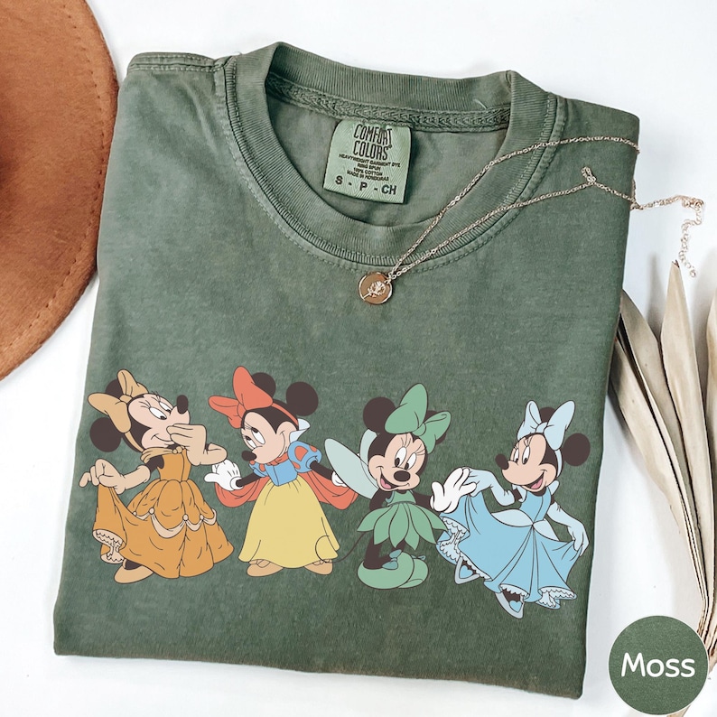 a green t-shirt with a graphic of Minnie Mouse and Snow White, along with a necklace and a brown hat.