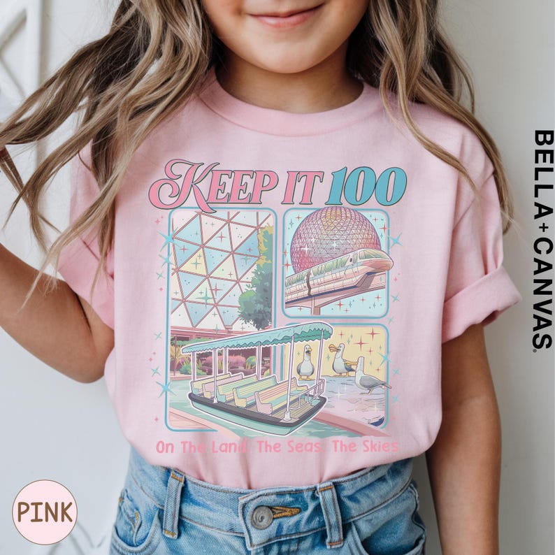 A young girl wearing a pink t-shirt with a graphic design featuring a Ferris wheel and a boat, along with the text "Keep it 100 On the land The sea The skies" printed on it.